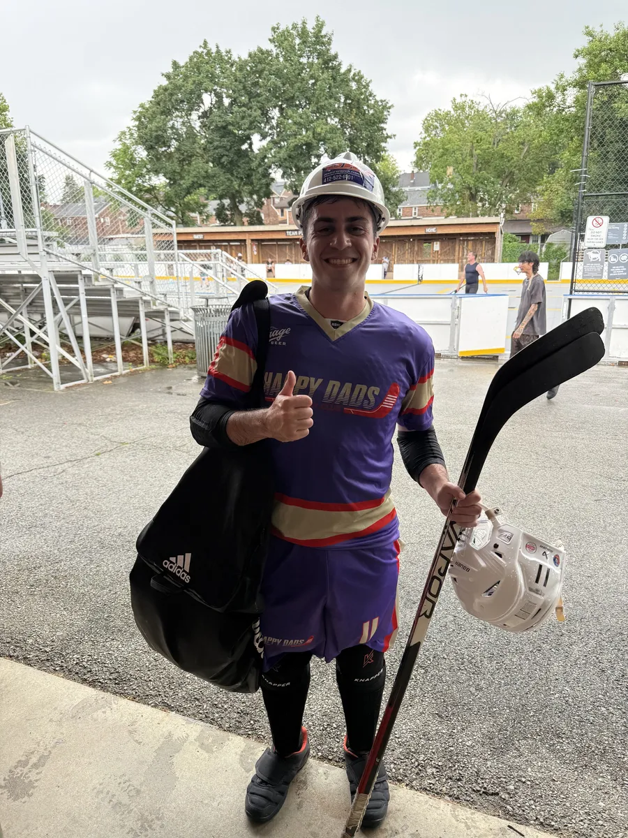Mark smiling with a thumbs up in the purple and gold Bridgeville Happy Dads jersey after a game in June 2026, holding his sticks and helmet.
